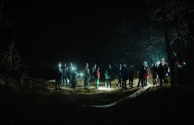 Skolotāji tumsā pulcējušies mežā ar gaismas lukturīšiem, lai dotos nakts pārgājienā