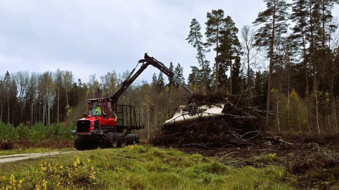 Pievedējtraktors krauj tehnoloģisko koksni apsegtā krautuvē meža ceļa malā