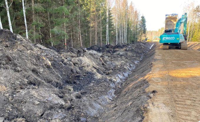 Mežā ekskavators rok grāvi un veido ceļa malu gar svaigi izbūvētu ceļu