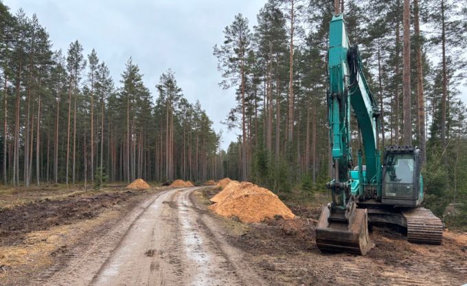Ekskavators ar vairākām grants kaudzēm stāv ceļa malā pirms ceļa būvniecības