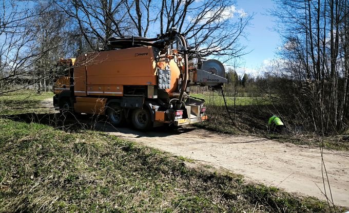 Uz meža ceļa stāv ar augstpiediena tehnoloģiju aprīkota mašīna, kura veic caurtekas tīrīšanu