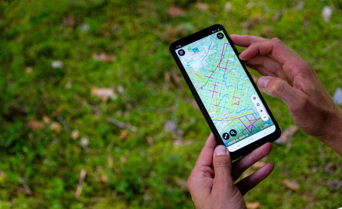 Cilvēks tur rokās telefona, kura ekrānā redzama LVM GEO mobilā lietotne, un tajā redzama karte ar atzīmētiem datiem